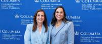 A photo of Kim Hekimian and Moneek Madra in blue blazers standing in front of a Columbia blue logo backdrop
